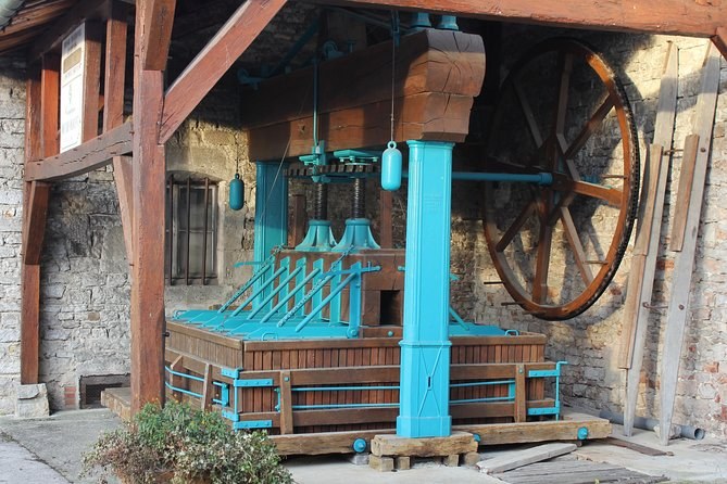 A tall old wooden wine press with a painted screw, under a timber roof
